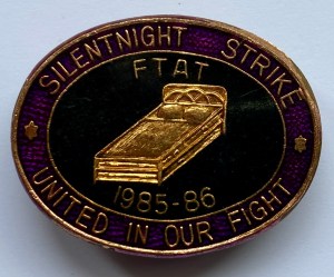 Oval badge. Purple outer ring with gold text: ‘Silentnight strike: united we fight.’ Inner black oval with a picture of a bed in gold and text: ‘FTAT 1985-86’