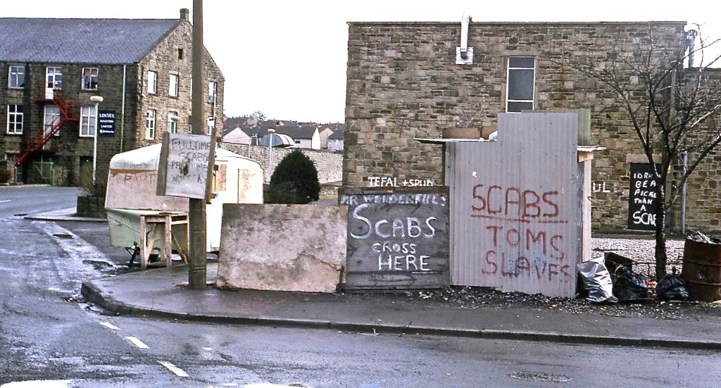 Industrials building with corrugated iron sheets to the front. Spray painted on the iron sheets are the words ‘Scabs: Tom’s slaves’.
